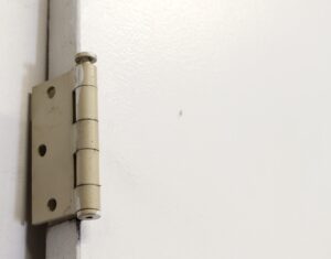 Close-up of a white wooden door hinge mounted on the door edge.
