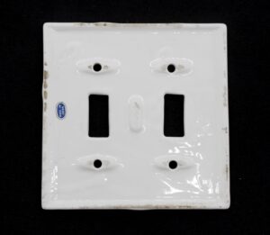 White ceramic two-gang switch cover with gold outlining, shown front on with two rectangular openings and four screw holes.