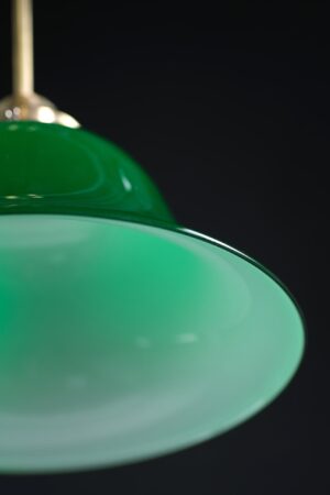 Close-up of a green encased glass pendant light with an antique brass pole, showing the curved shade and part of the fixture against a dark background.