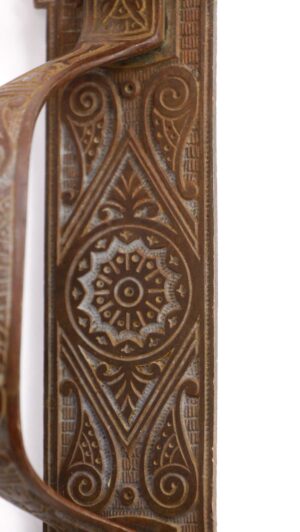 Ornate bronze left-hand door pull with a thumb latch and detailed carved pattern.