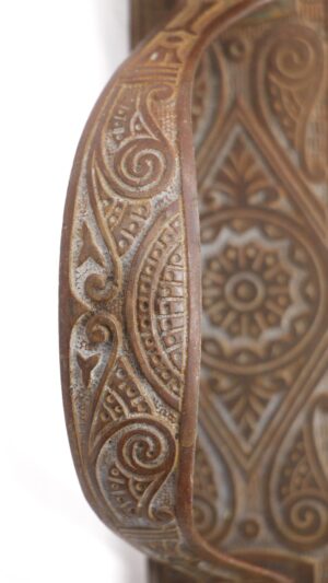 Close-up of an antique bronze left-hand door pull with ornate carved detailing and a curved thumb latch.