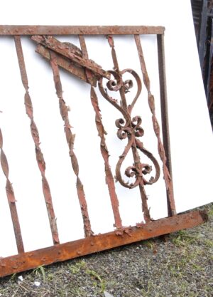 Heavily rusted wrought iron fire escape balcony front with ornate scrollwork and chipped paint, shown at a slight angle with bent vertical bars and top and bottom rails visible.