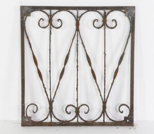 Antique wrought iron panel with curls and swirls in a rectangular frame, showing rust and age marks.
