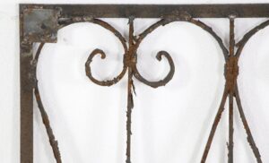 Close-up of an antique wrought iron panel with curls and swirls in a solid frame, showing rust and age-related wear.