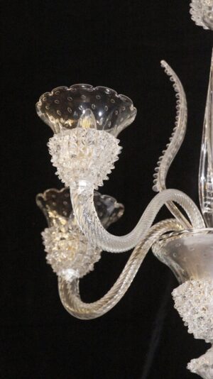 Close-up of a clear glass chandelier arm with a rostrato glass bowl and a scalloped shade detail against a dark background.