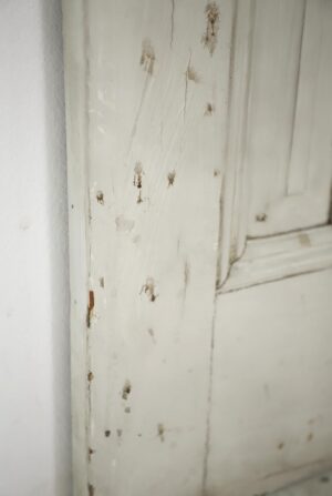 White painted passage door with five panels, shown close up with chipped paint and surface wear along the frame edge.