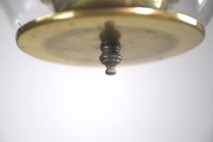 Close-up of the underside of a brass lantern light, showing a central candlestick socket beneath a round plate and clear glass shade above.
