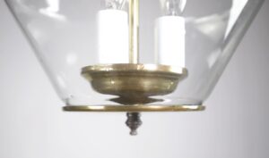 Close-up of a clear glass lantern light with an antique brass body and two visible candlestick sockets.