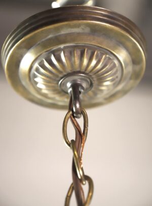Close-up of a pendant light canopy with an antique brass finish, showing the chain fitter and twisted cord connection.