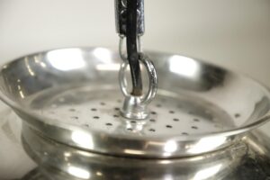 Close-up of a stainless steel colander pendant light with a hanging chain and perforated bowl shape.