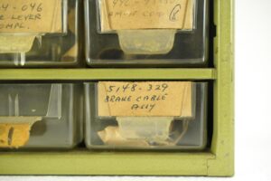 Close-up of a clear plastic parts drawer with handwritten paper labels in a green metal stackable storage rack.