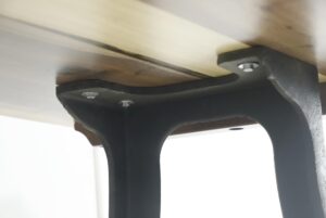 Close-up of a dining table underside showing a walnut top secured to a black cast iron leg with visible bolts.