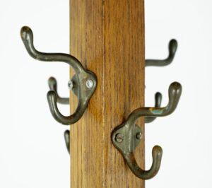 Close-up of a dark wood coat rack with four cast iron hooks, showing one hook mount with different screws.