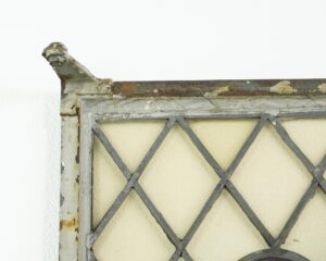 Close-up of the corner of a steel framed casement window with leaded criss cross glass, showing chipped white paint and rust on the frame.