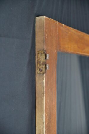 Close-up of a vintage pine wood passage door frame with a clear glass panel, showing the hinge area and visible surface wear on the dark wood tone frame.