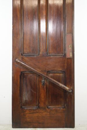 Antique wooden double door with four vertical panels and a diagonal handrail, shown in a front view with visible wear at the bottom.