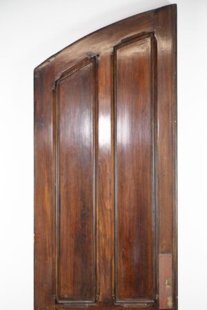 Antique wooden arched double door with four vertical panels and visible damage near the bottom edge.