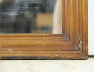 Close-up of a rectangular wall mirror with a medium wood tone frame showing minor surface wear at the corner.