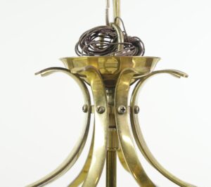 Close-up of an antique brass chandelier frame with curved arms, visible screws, and the upper section of the drum-shaped glass enclosure.