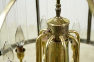 Close-up of a traditional drum chandelier with an antique brass frame and clear beveled glass panels, showing the central top section and surrounding candle-style arms.
