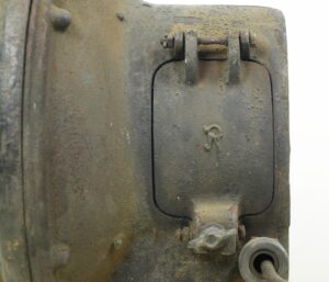 Close-up of a steel flood light with a hinged access panel, clamp hardware, and a visible cord fitting.