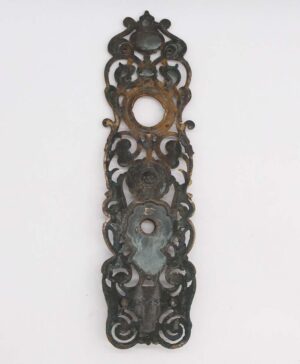 Antique Victorian bronze door back plate with ornate cutout details and a central keyhole opening.