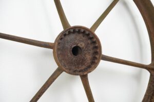 Close-up of a reclaimed cast iron wagon wheel showing the six spokes and rusted center hub.