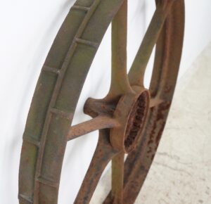Close-up of a cast iron wagon wheel with six spokes and surface rust.