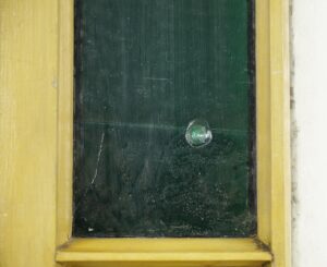 Close-up of a Queen Anne stained glass window panel in an antique pine frame, showing the green glass section and worn frame edge.