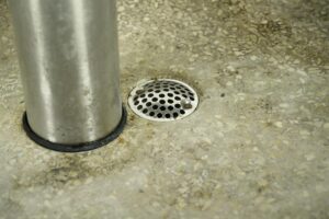 Close-up of a gray and white metal hand wash fountain showing the foot control column and circular drain.