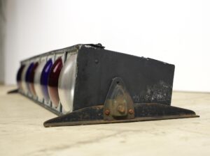 Vintage stage light with a steel frame and round red, white, and blue lenses, shown from the side with visible wear.