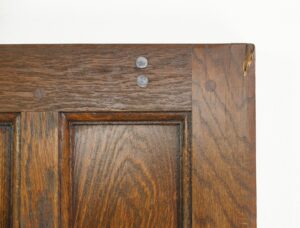 Close-up of the upper corner of a dark wood oak entry door with paneled construction and visible wear at the edge.