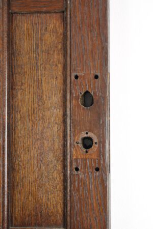 Close-up of an Arts and Crafts oak door edge showing the lock bore and screw holes in the dark wood grain.