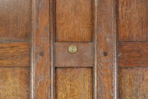 Close-up of a dark wood tone oak door panel with vertical and horizontal muntins and a small round peephole in the center section.