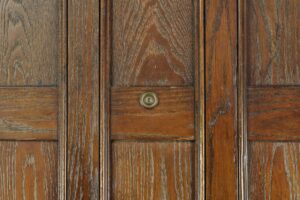 Close-up of a dark wood tone oak entry door with vertical panels, a centered peephole, and visible grain and wear.