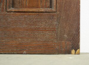 Close-up of a dark wood Arts and Crafts entry door showing the lower corner, panel molding, and worn oak grain.