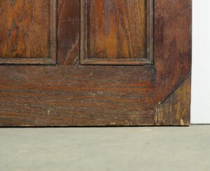 Close-up of the lower section of a dark oak entry door with Arts and Crafts paneling and visible age wear along the wood grain and edges.