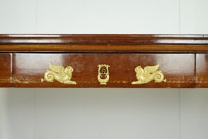 Close-up of a mahogany desk drawer with gilt bronze griffin appliques and a central keyhole escutcheon.
