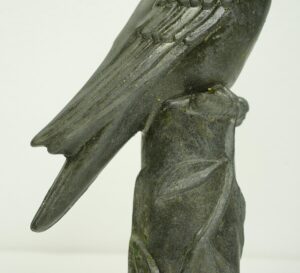 Close-up of a black bronze woodpecker statue perched on a leafy log, showing the bird’s wing and body detail.
