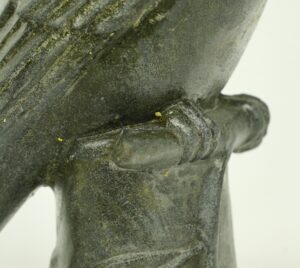 Close-up of a black bronze woodpecker statue showing the bird perched on a leafy log with visible age wear and a textured surface.