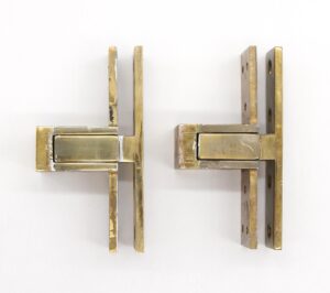 Pair of traditional Harmon pocketed pivot door hinges in polished brass, shown as a matching pair with visible age wear and mounting holes.