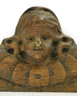 Close-up of a reclaimed oak cherub head carving with visible wear and a broken-off nose.