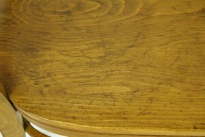 Close-up of a medium wood tone chair seat with visible wear and scratches.