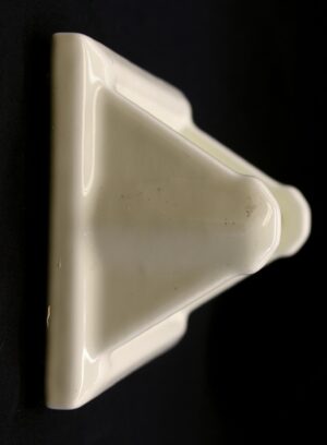 Pale yellow ceramic flush mount toilet paper holder shown in close-up, with a glossy porcelain finish and visible surface wear.