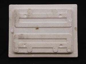 Back view of a ceramic flush mount toilet paper holder with visible mounting tabs and surface wear.