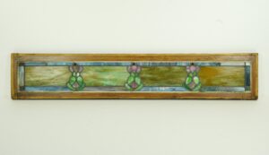 Art Nouveau stained glass window in a light wood pine frame, shown horizontally with three green and pink leaded motifs across textured multicolor panes.