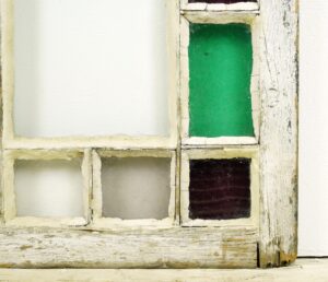 Close-up of an Antique Queen Anne stained glass window with textured clear, white, green, and dark panes in a worn pine frame.