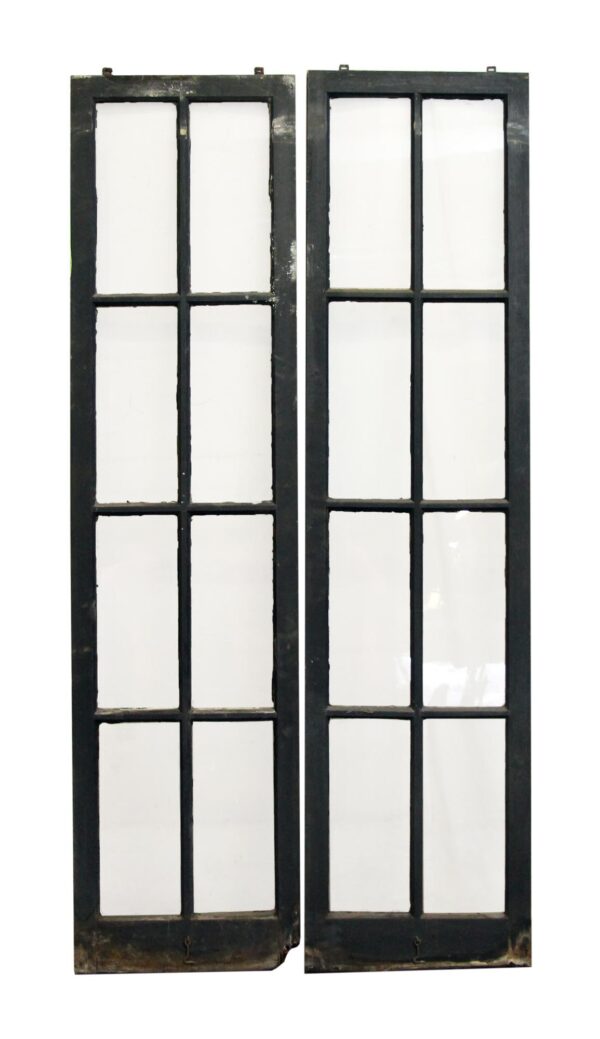 Two tall narrow black wood windows with eight panes each are shown side by side, and one pane appears cracked while the lower edge shows visible wear and water damage.