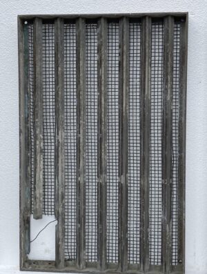 Bronze window grate with vertical bars and woven mesh screen, shown front on with a small cutout in the lower left corner.