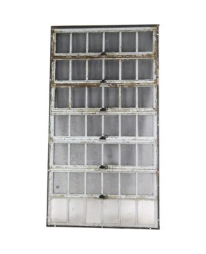 Industrial encasement window with a heavy steel frame and seven hinged sections of textured glass panes, shown full length with visible wear and some cracked panes.